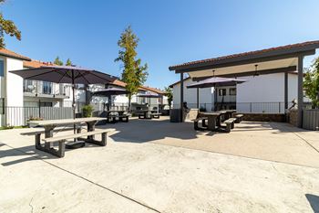 a patio with picnic tables and umbrellas in front of a building at Alturas Paso Robles Apartment Homes, Paso Robles, CA